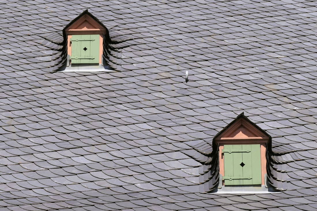 Licensed stock photograph: a slate roof covered in overlapping scalloped courses, with two small shuttered dormer windows set into the slope.